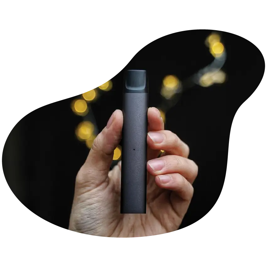 Hand holding a sleek black cannabis vape pen with blurred string lights in the background.