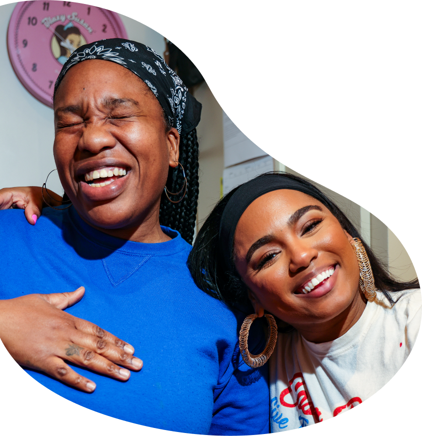 Two women smiling and laughing together inside a Housing Works Cannabis Co. community space.