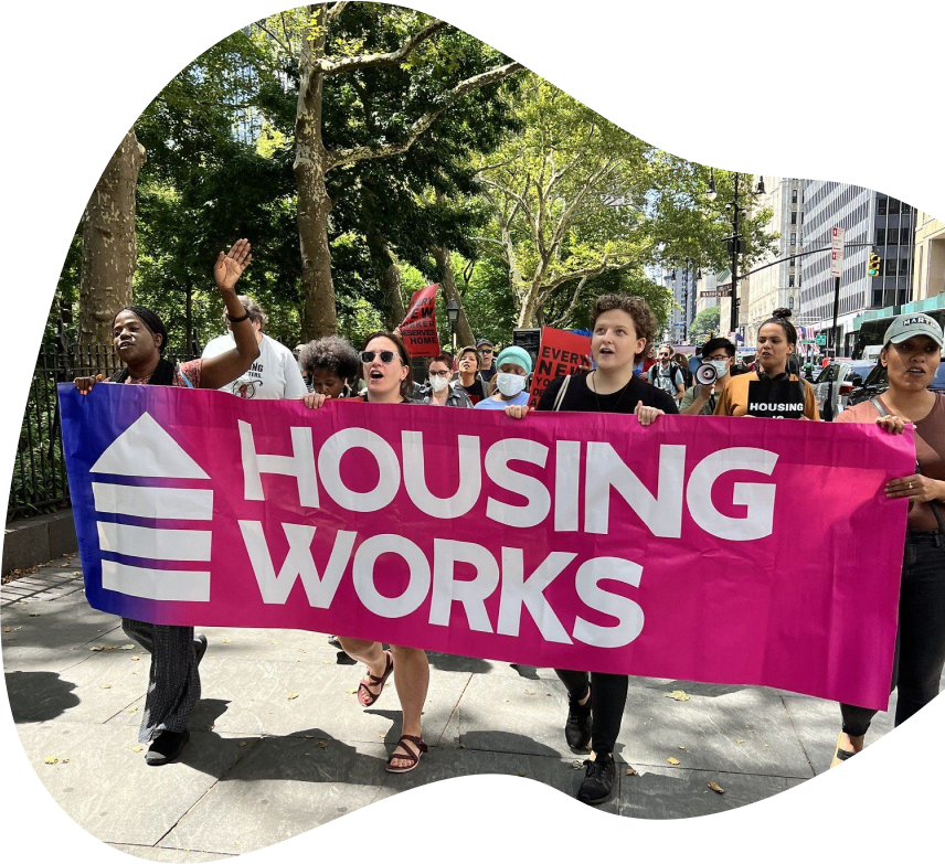 Group of activists marching with a bright pink Housing Works banner during a city protest, highlighting the organization’s advocacy and community engagement.
