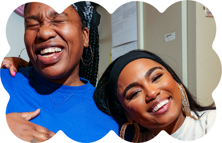 Two women smiling and laughing together inside a Housing Works Cannabis Co. community space.