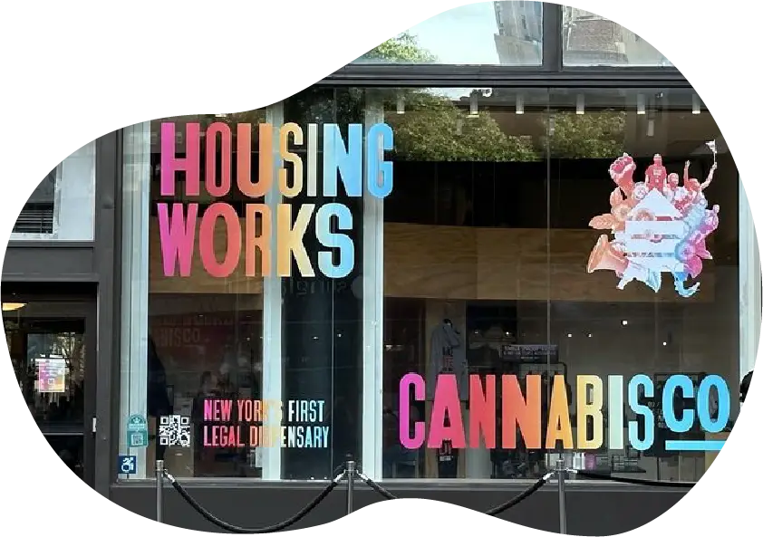 Storefront window of Housing Works Cannabis Co., New York’s first legal cannabis dispensary, with colorful text signage and abstract artwork.