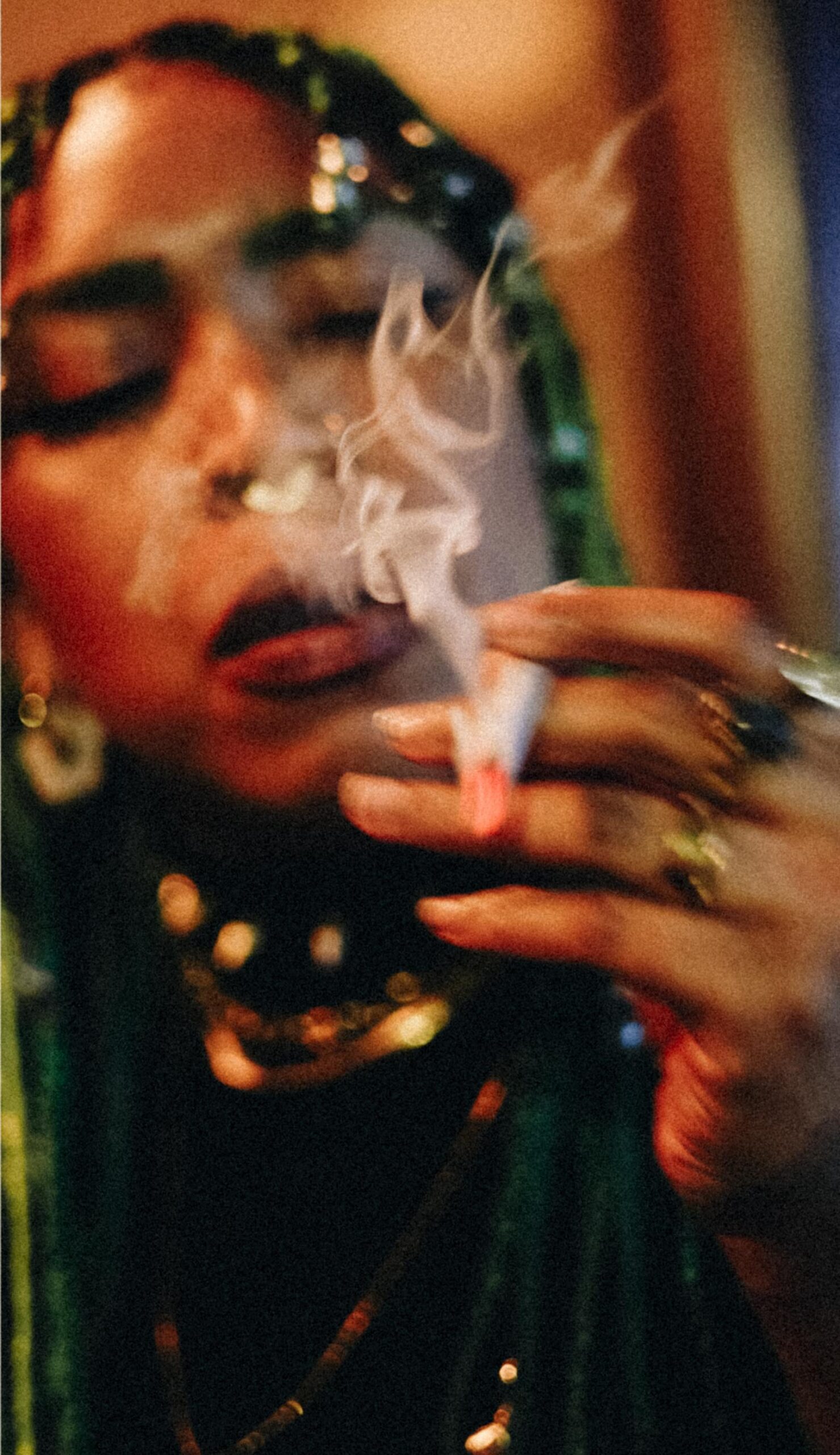 Person smoking a lit cannabis joint as smoke rises around their face.